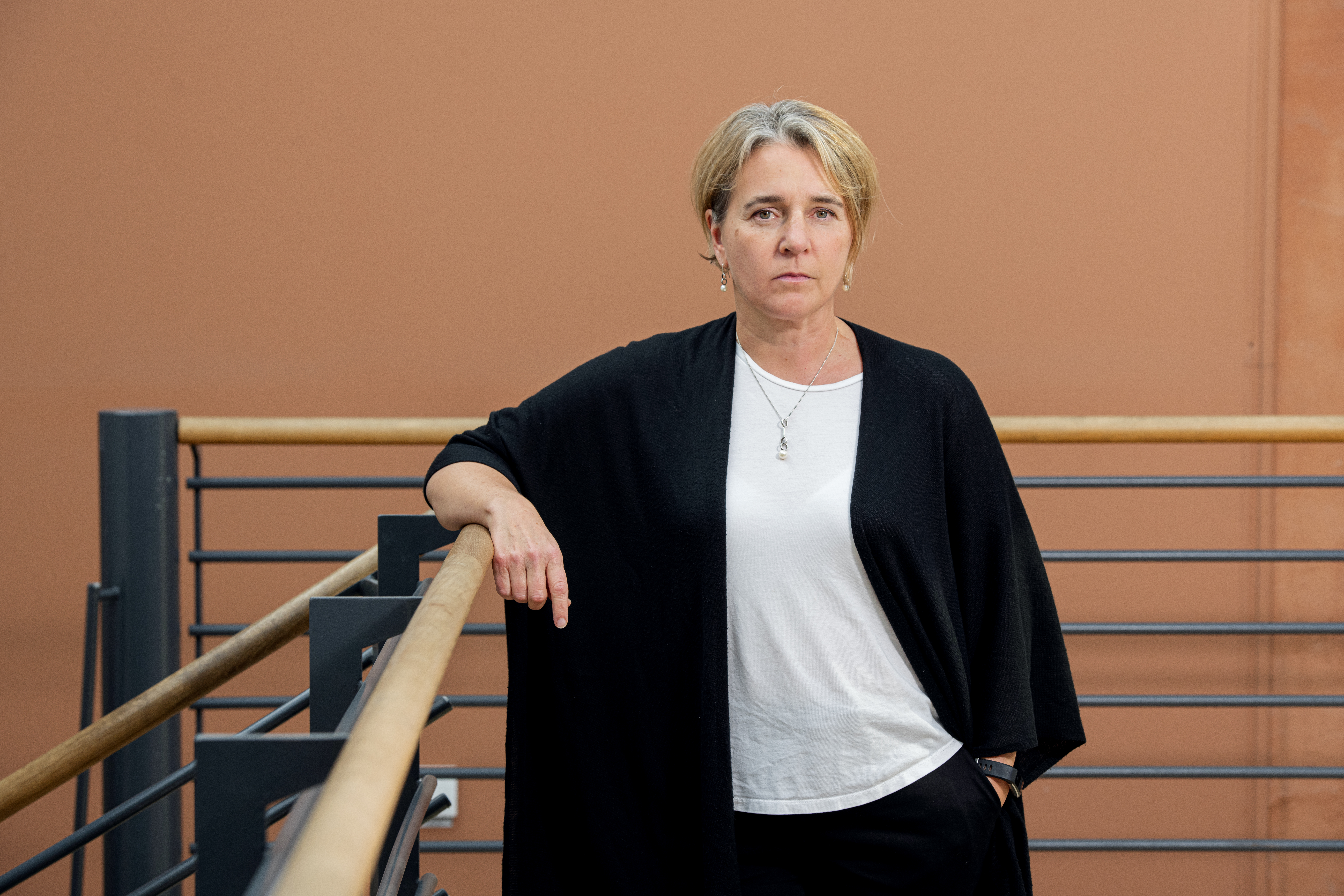 Pressbild Rebecka Svensén. Rebecka ser bister ut, hon står vid ett räcke framför en rostorange vägg.