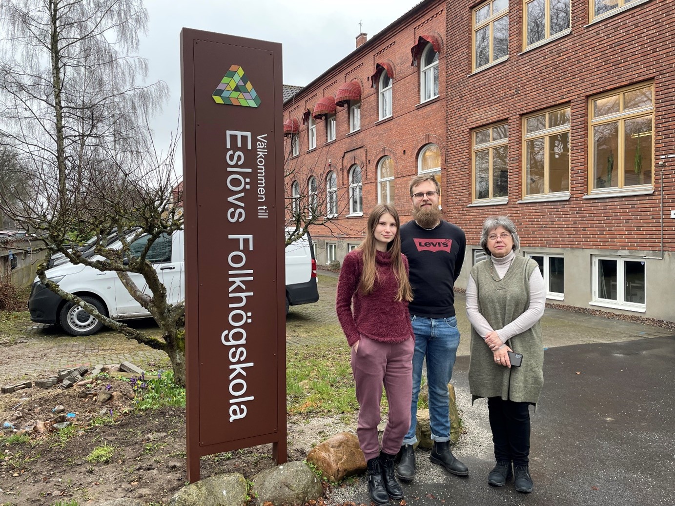 Deltagare och personal framför skylt för Eslövs folkhögskola. 