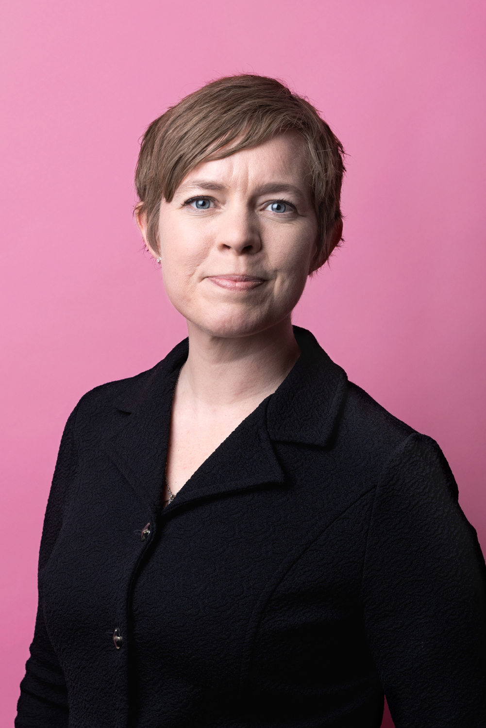 Porträttbild Lisa Minnhagen. Lisa har kort brunt hår och tittar rakt in i kameran.