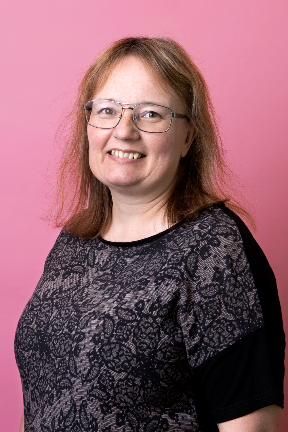 Porträttbild Carolina Thulin. Carolina står vinklad mot kameran och ser glad ut. hon har en grå, mönstrad top på sig.