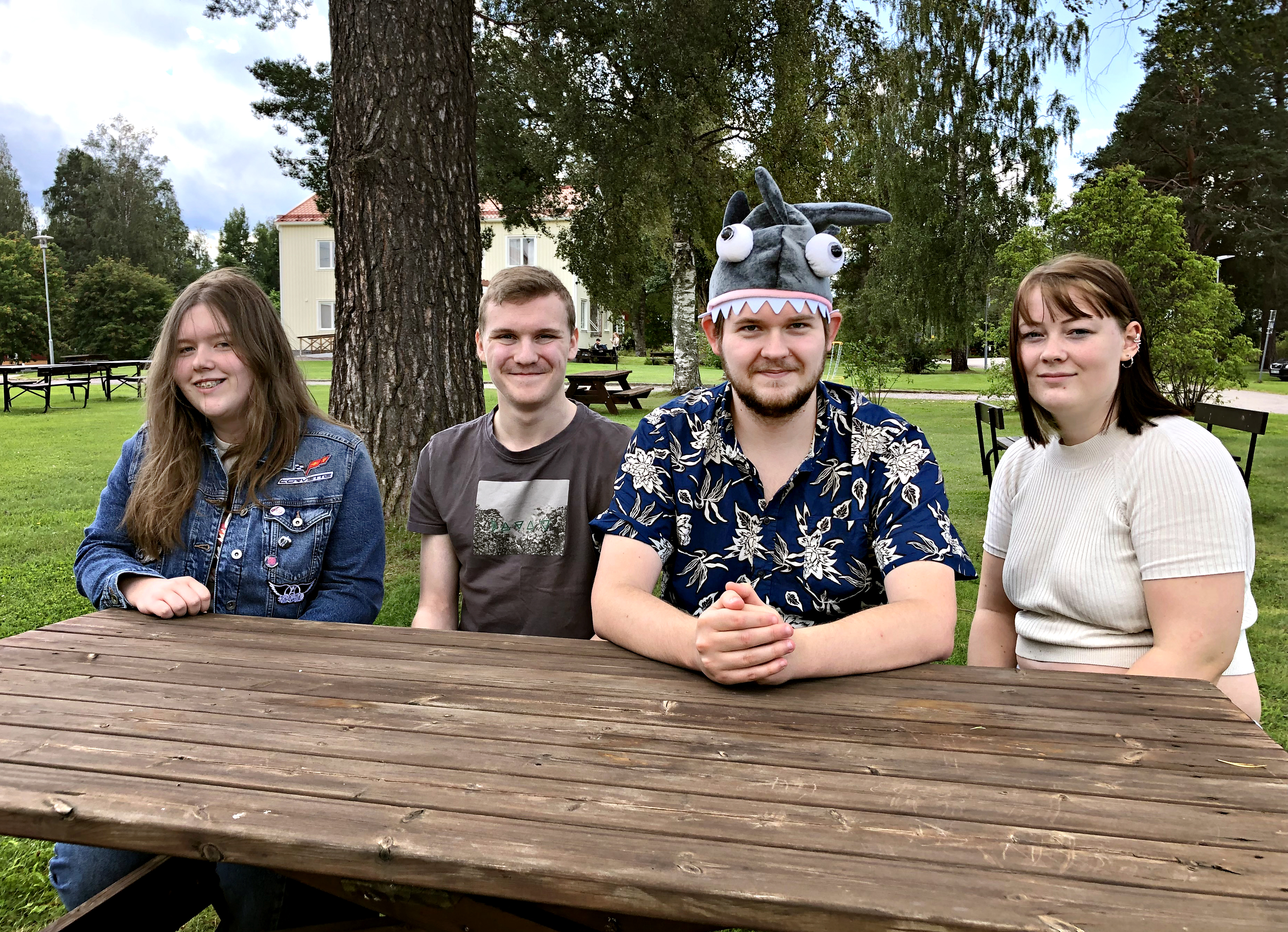 Deltagare på dataspelskursen på Hola folkhögskola sitter på en bänk med skolan i bakgrunden.