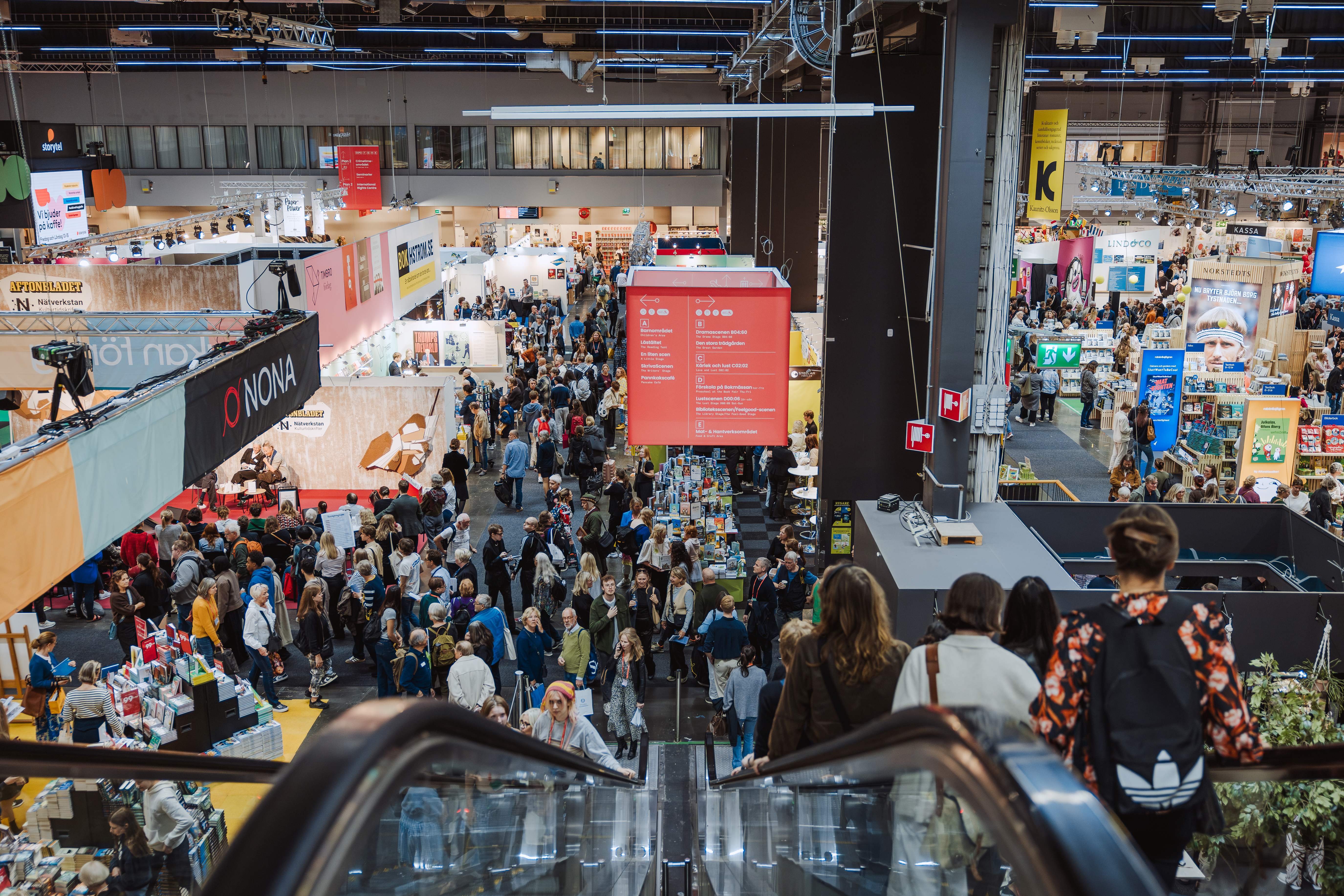 Bild inifrån Bokmässan. I förgrunden toppen på en rulltrappa, nedan syns montrar och ett myller av människor.