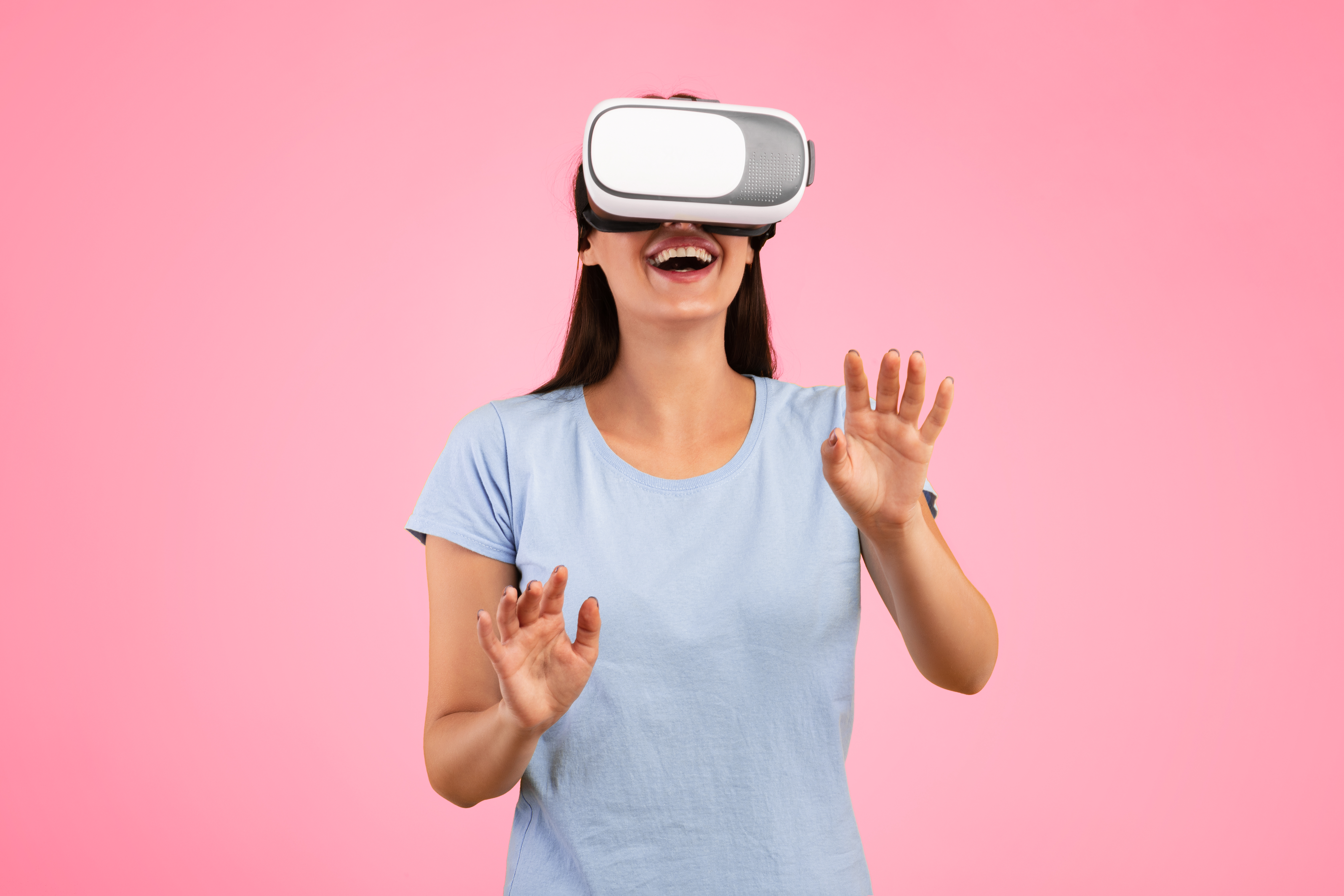 Kvinna med VR-headset mot rosa bakgrund. Kvinnan är glad och famlar med händerna. 