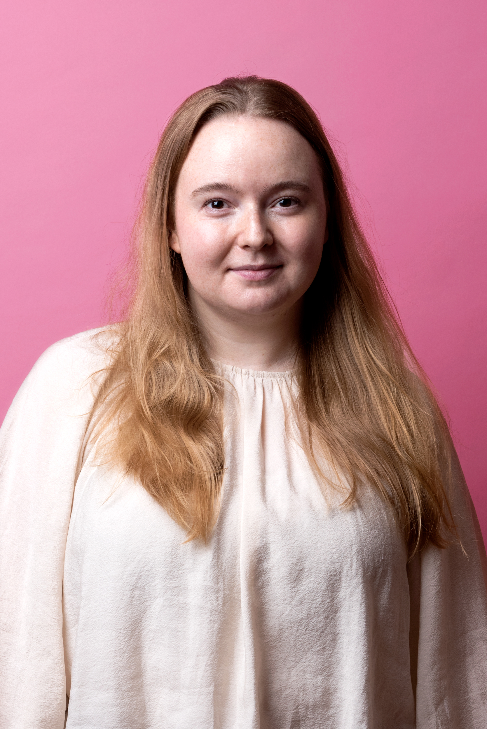 Sofia tittar rakt in i kameran, hon är iklädd en vit topp. Hennes hår faller ner över axlarna.