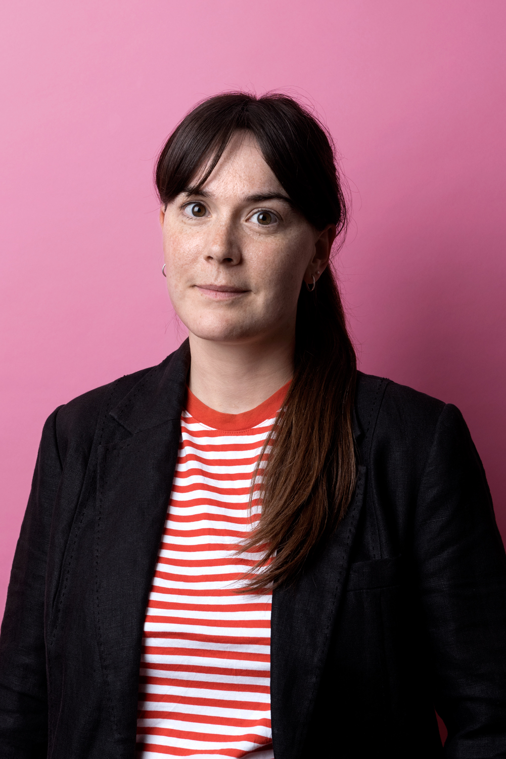 Porträttbild av Rebecka Svenberg. Rebecka har mörkt hår, kavaj och randig t-shirt. 