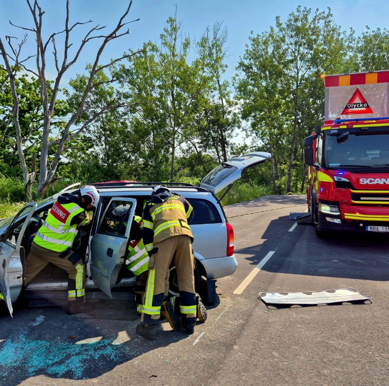 Två räddningsarbetare som jobbar i en nödsituation i en bil, i bakgrunden står en brandbil.