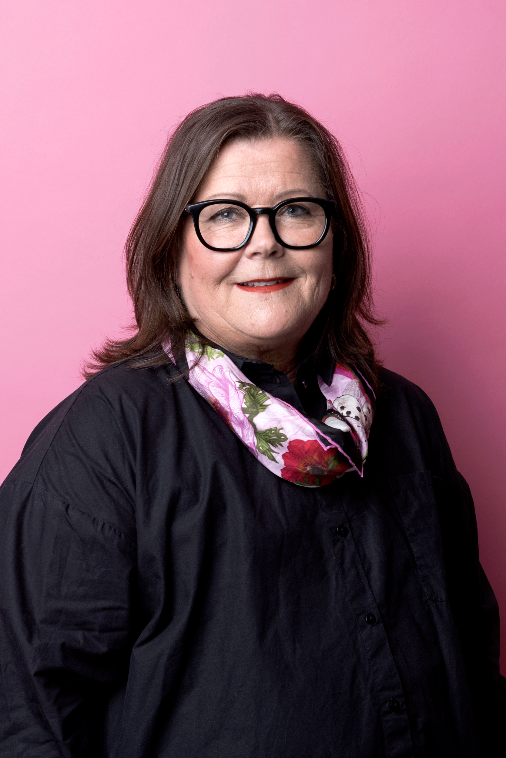 Porträttbild Annika Jansson. Annika har mörkt halvlångt hår och glasögon. Hon bär en svart blus och färgglad scarf, tittar in i kameran och ler.