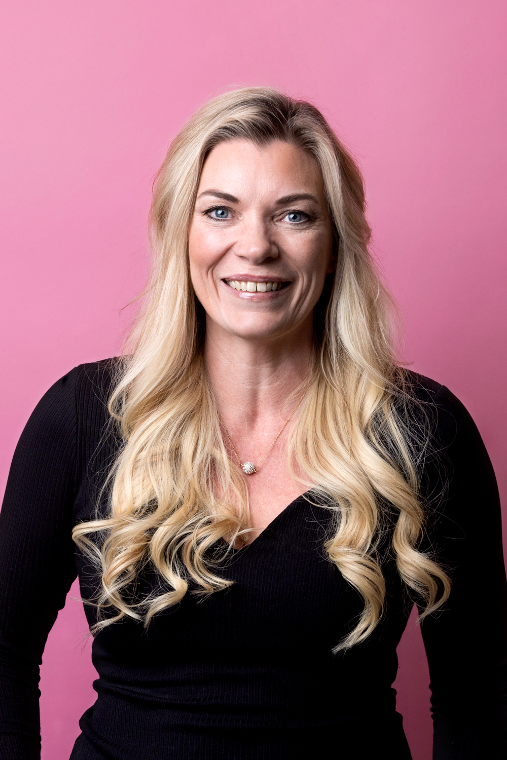 Porträttbild Kajsa Borgström. Kajsa har långt blont lockigt hår, hon tittar rakt in i kameran och ser glad ut.