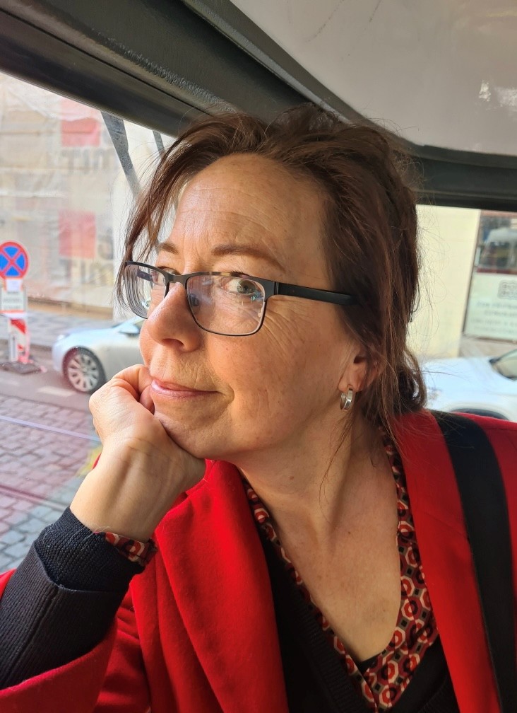 Anna-Karin sitter i en bil, hon lutar huvudet i handen och tittar snett in i kameran med ett litet leende.