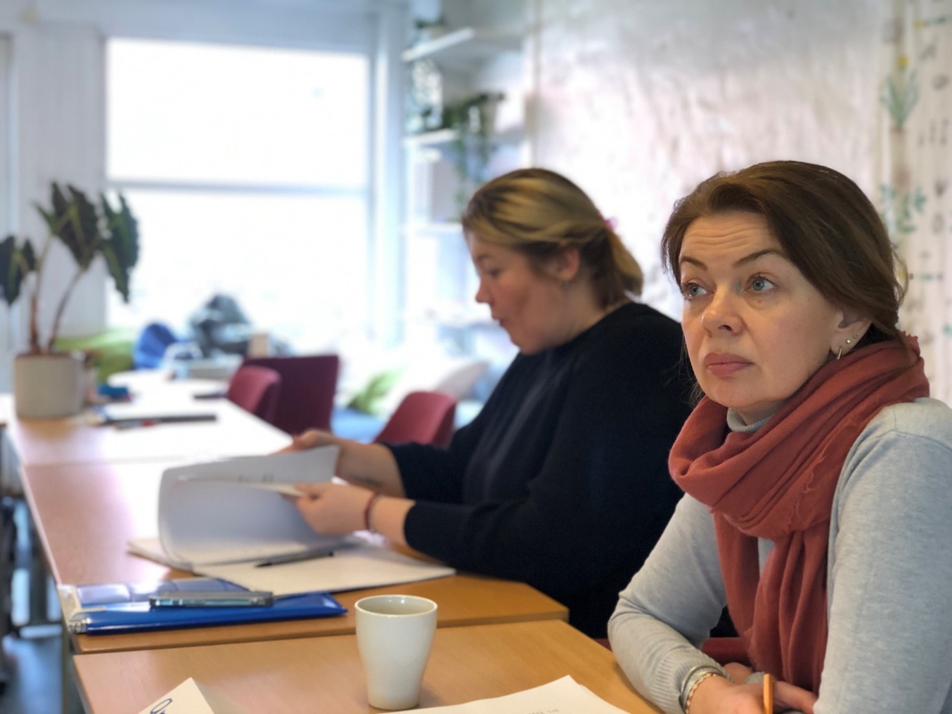 Deltagare i Care-verksamhet sitter i utbildningslokal, dricker kaffe och bläddrar i studiematerial.