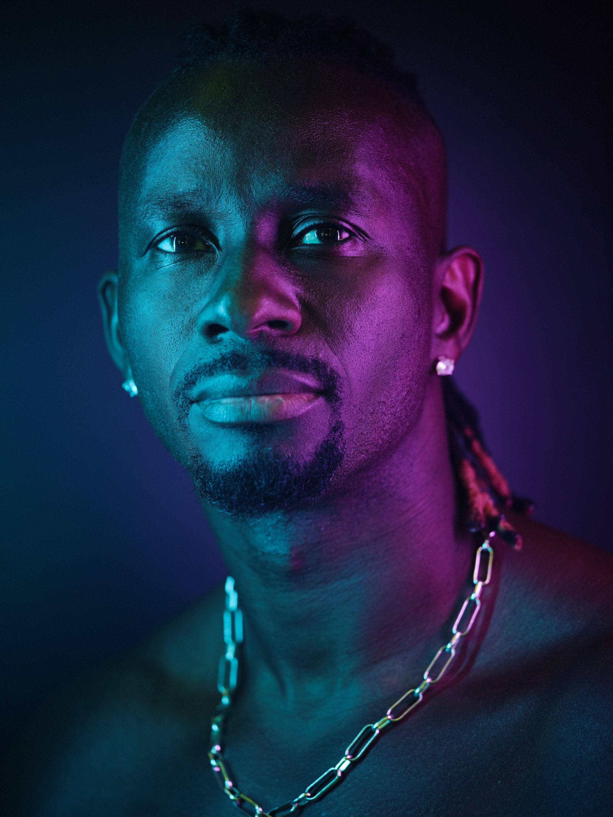 Pa Modou Badjie porträtt i mörka toner, hans ansikte lyses upp av blått och lila ljus.