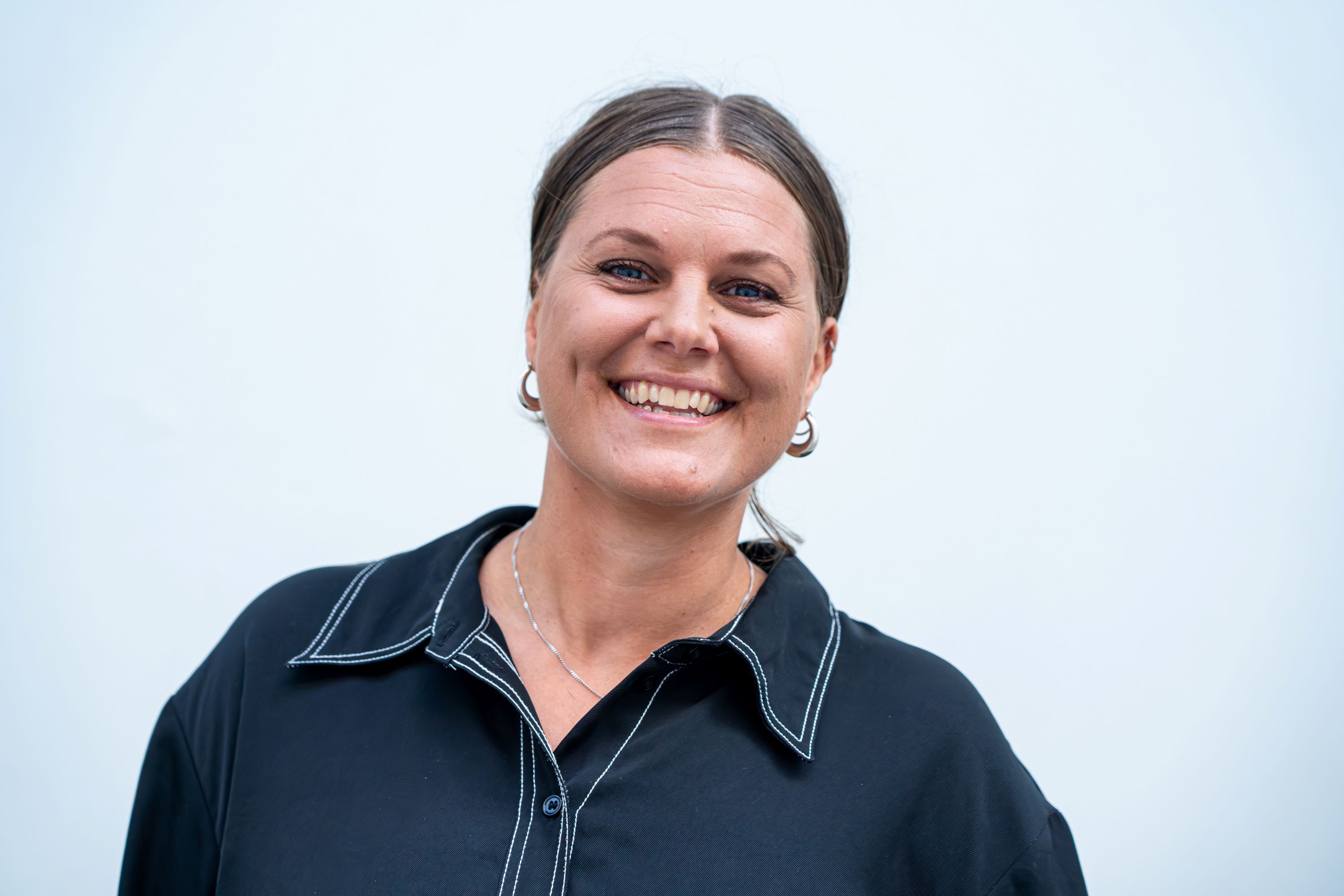 Porträttfoto av Clara Bankefors mot ljus bakgrund. Clara ler stort och är klädd i en mörk skjorta.
