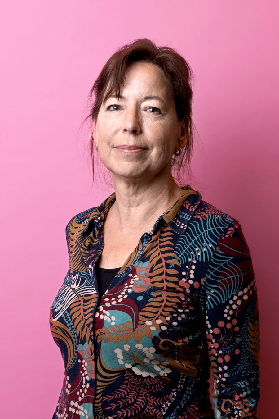 Porträttfoto av Anna-Karin Lindblom. Anna-Karin har uppsatt hår och en färgglad blus.