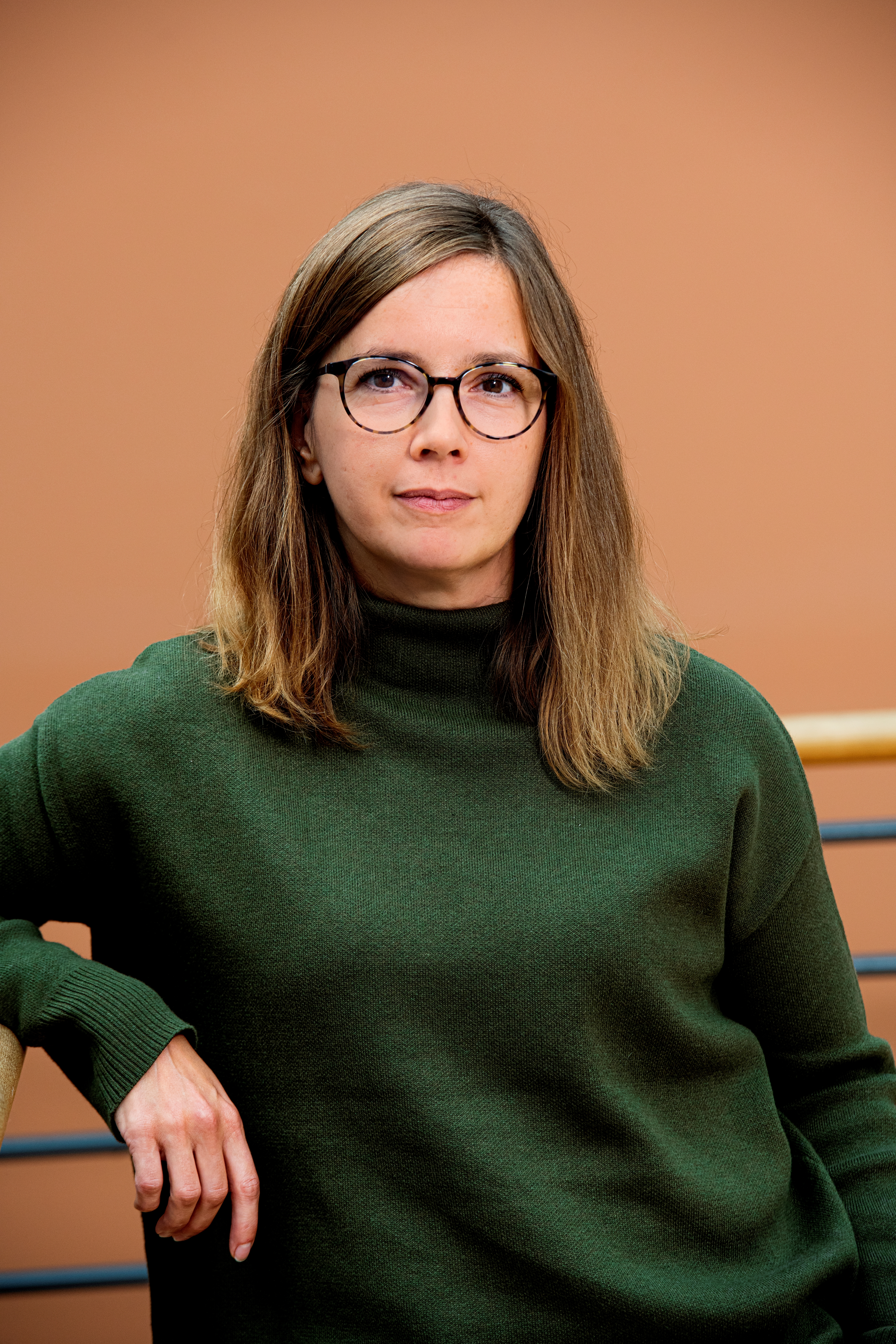 Pressbild Linda Stridsberg. Hon har en mossgrön kofta på sig, medellångt brunt hår och glasögon. Hon tittar rakt in i kameran.